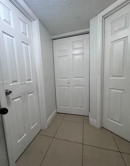 hall featuring light tile patterned flooring, baseboards, and a textured ceiling