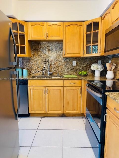 kitchen with light tile patterned floors, stone counters, decorative backsplash, black appliances, and a sink