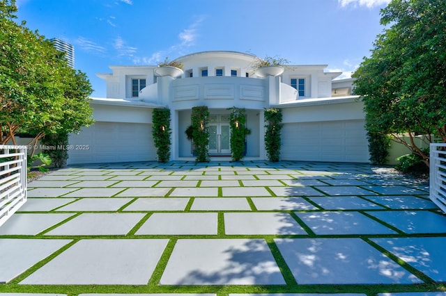 art deco house with a balcony, fence, an attached garage, stucco siding, and french doors