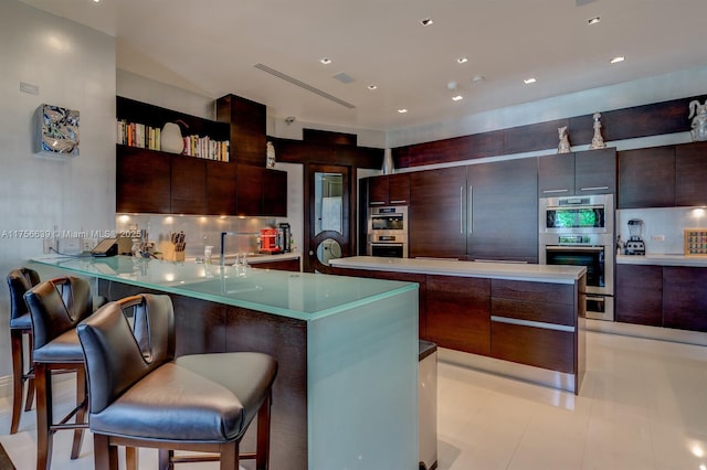 kitchen with decorative backsplash, double oven, modern cabinets, and a kitchen bar