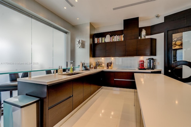 kitchen with a peninsula, a sink, light countertops, dark brown cabinets, and modern cabinets