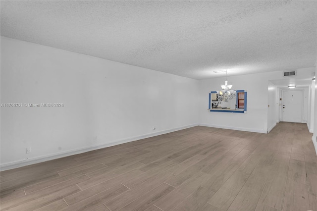 spare room with wood finished floors, baseboards, visible vents, a textured ceiling, and a chandelier