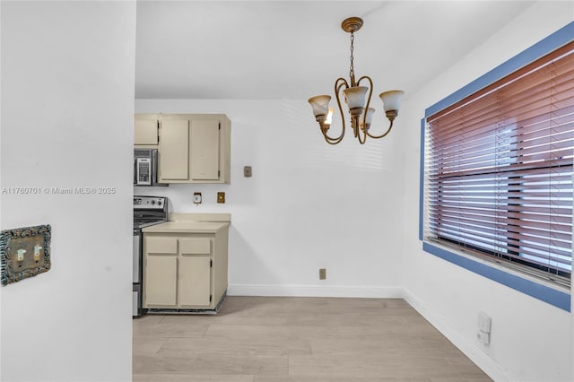 kitchen with baseboards, light countertops, electric stove, cream cabinets, and a notable chandelier