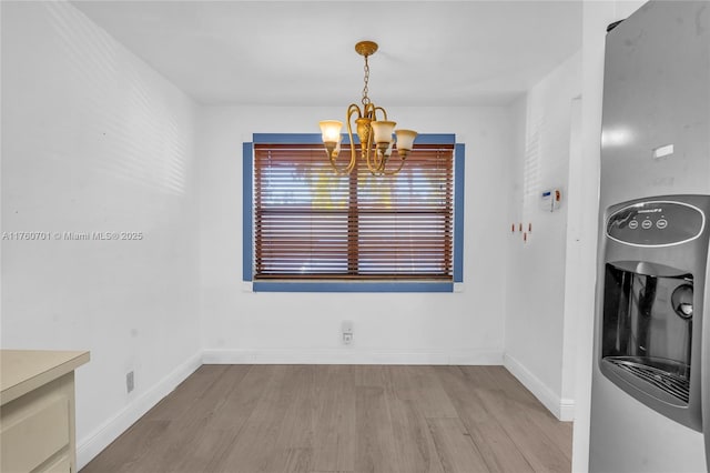 unfurnished dining area with wood finished floors, baseboards, and a chandelier