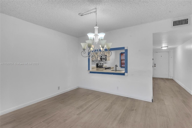 empty room with an inviting chandelier, wood finished floors, visible vents, and a textured ceiling