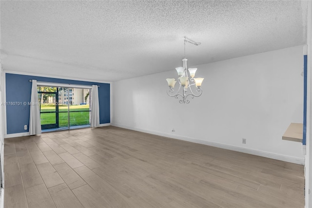 unfurnished room featuring an inviting chandelier, wood finished floors, baseboards, and a textured ceiling