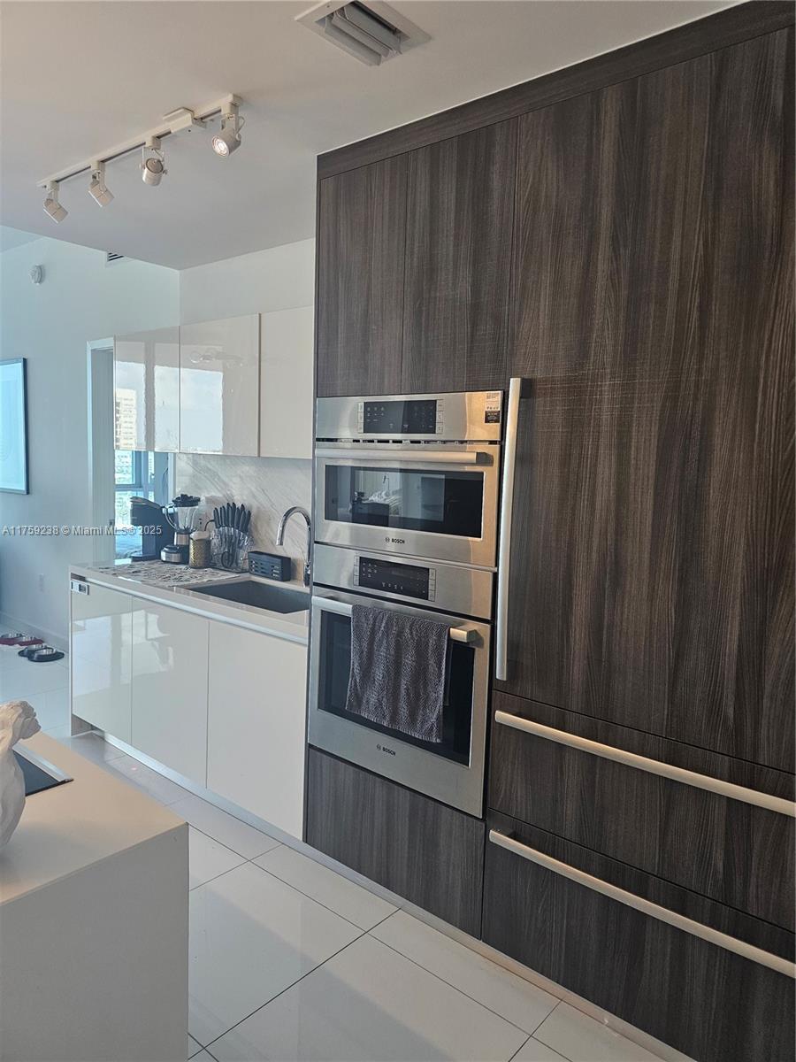 851 NE 1st Ave Unit 1408, Miami, FL 33132 - kitchen with stainless steel double oven, dark brown cabinetry, modern cabinets, rail lighting, and light countertops