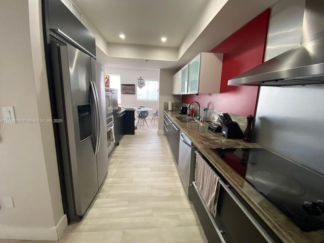 kitchen featuring recessed lighting, a raised ceiling, stainless steel appliances, wall chimney exhaust hood, and a sink