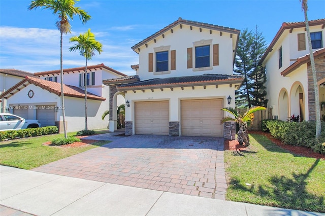 mediterranean / spanish-style home featuring decorative driveway, stone siding, a front yard, and an attached garage