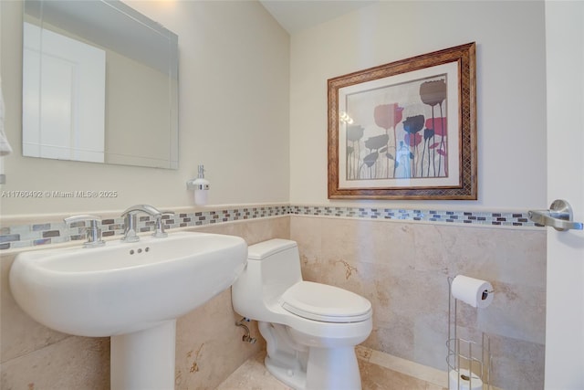 half bath featuring tile walls, toilet, and wainscoting