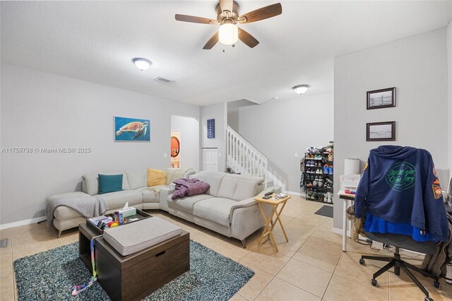 living area featuring light tile patterned flooring, ceiling fan, stairs, baseboards, and visible vents
