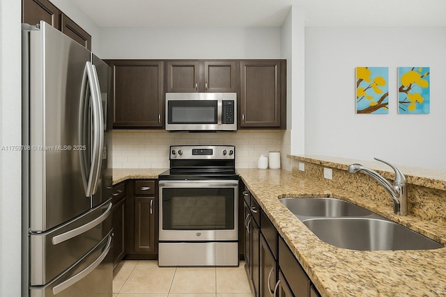 kitchen featuring dark brown cabinets, light stone counters, a sink, appliances with stainless steel finishes, and backsplash