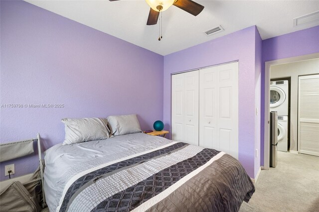 bedroom featuring ceiling fan, stacked washer / dryer, visible vents, a closet, and light carpet