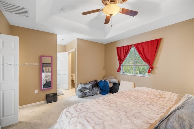 carpeted bedroom with ceiling fan, visible vents, baseboards, ensuite bathroom, and a tray ceiling