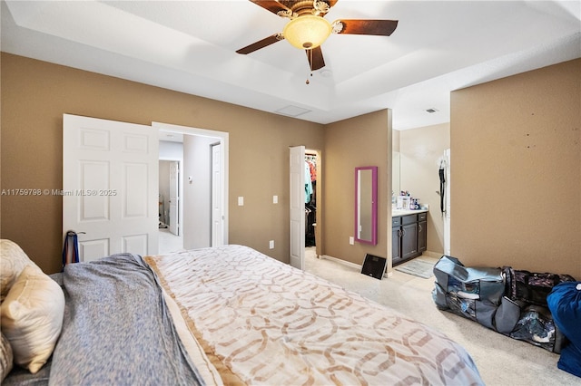 bedroom featuring ceiling fan, light colored carpet, a raised ceiling, a spacious closet, and ensuite bath