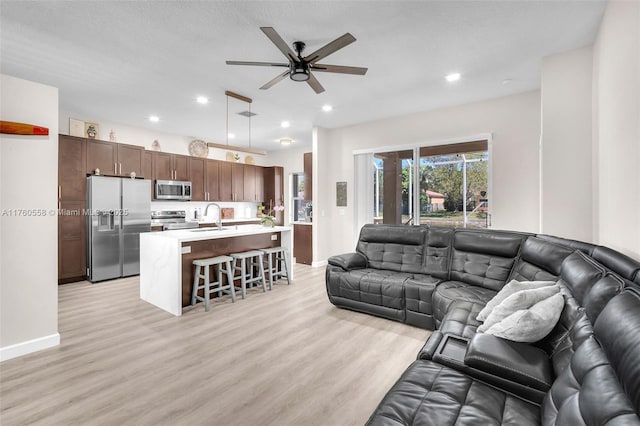 living room with light wood-type flooring, a ceiling fan, a textured ceiling, recessed lighting, and baseboards