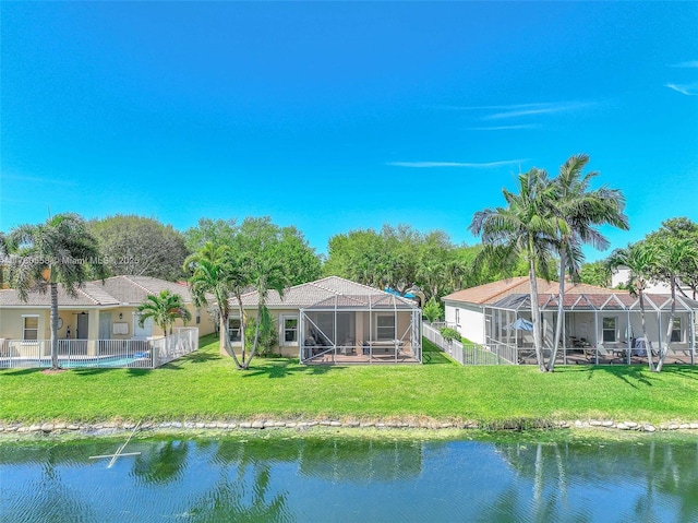 rear view of house with a lanai, a lawn, fence, and a water view