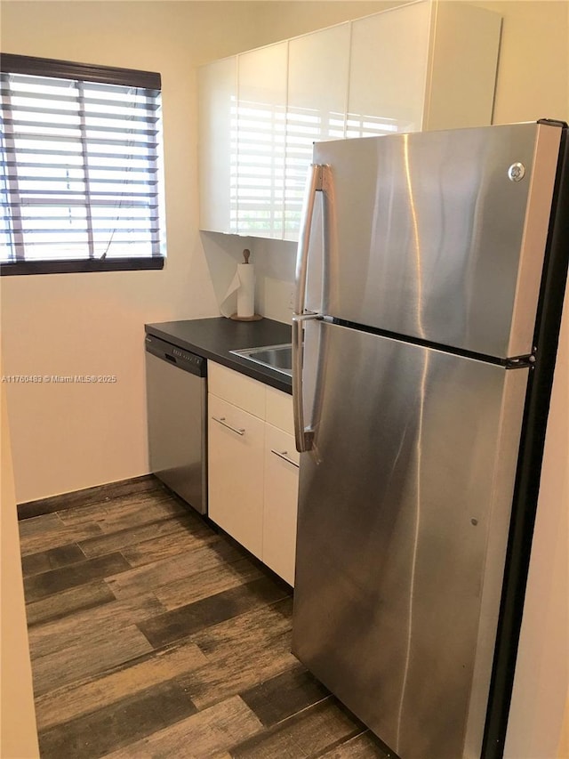 kitchen with dark wood-style flooring, a sink, appliances with stainless steel finishes, white cabinetry, and dark countertops