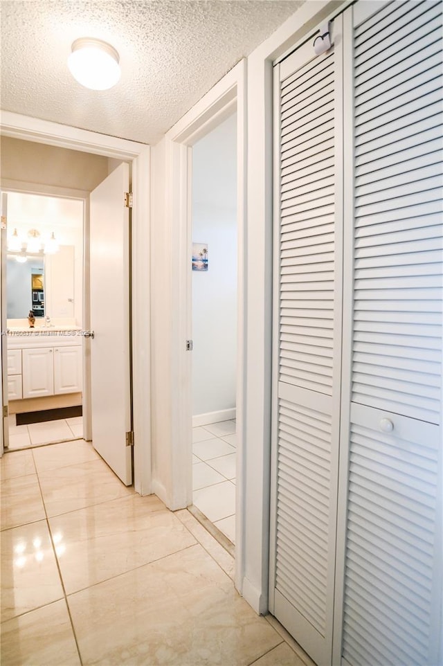 hallway featuring light tile patterned flooring, a textured ceiling, and baseboards