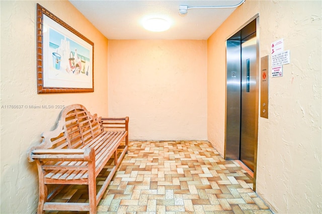 hall featuring elevator, a textured wall, and brick floor