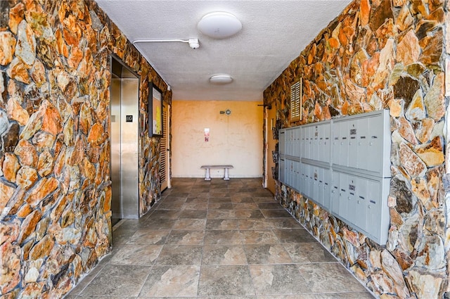 corridor featuring mail area, stone finish flooring, elevator, and a textured ceiling