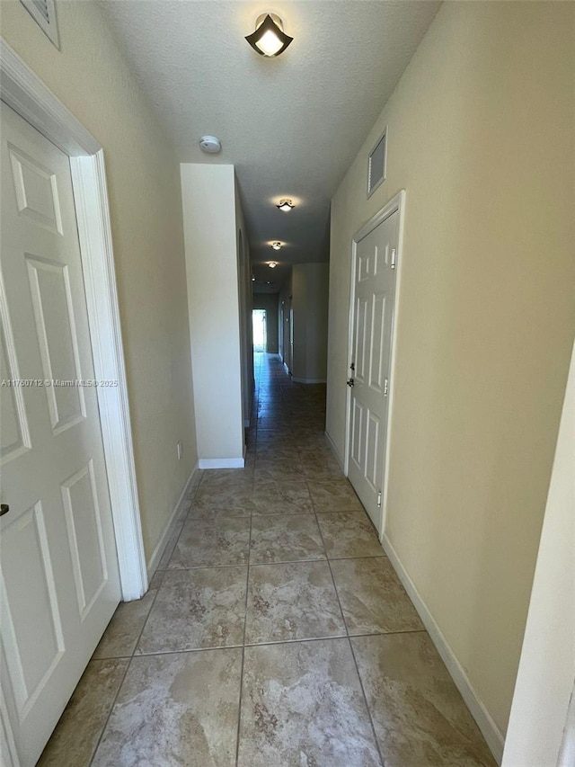 hall featuring light tile patterned floors, visible vents, a textured ceiling, and baseboards