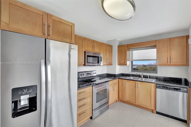 kitchen with light tile patterned floors, appliances with stainless steel finishes, dark stone counters, and a sink