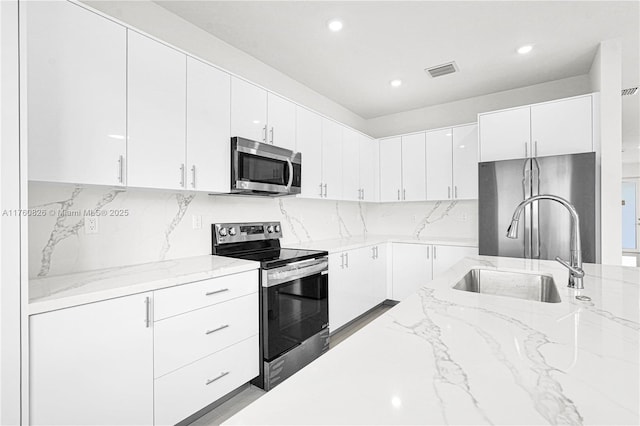 kitchen with visible vents, a sink, light stone counters, appliances with stainless steel finishes, and white cabinets