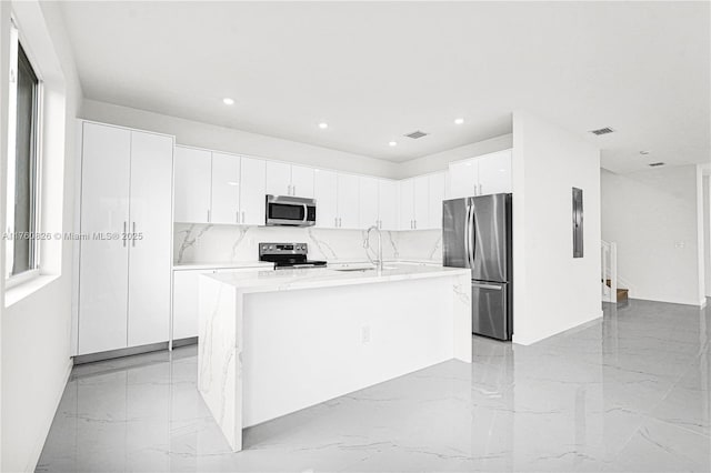 kitchen featuring a center island with sink, visible vents, stainless steel appliances, white cabinetry, and marble finish floor