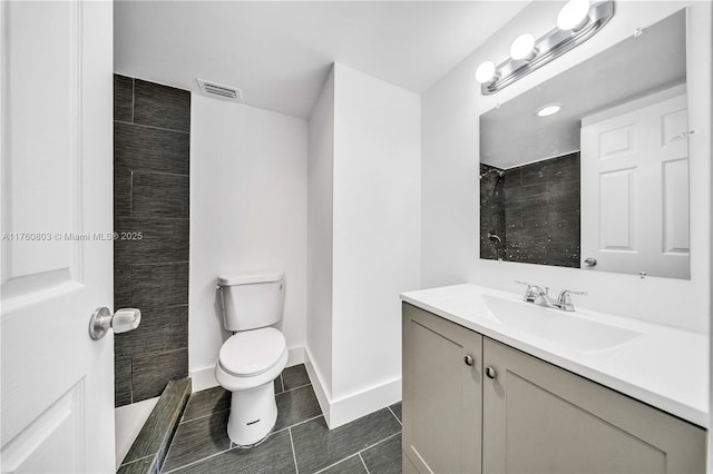 bathroom with vanity, baseboards, visible vents, a tile shower, and toilet