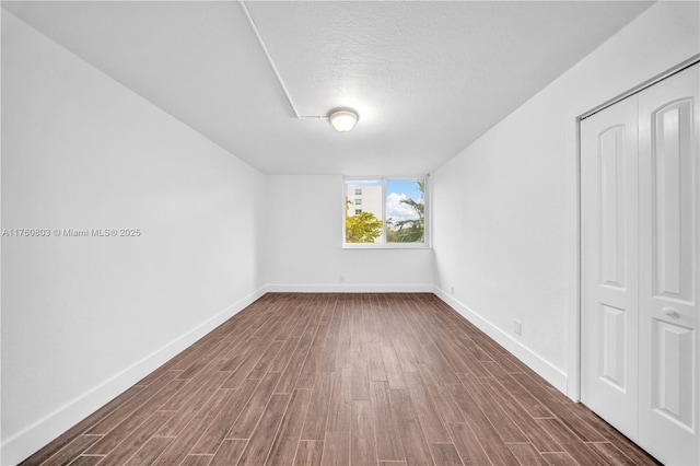 additional living space with a textured ceiling, dark wood-type flooring, and baseboards