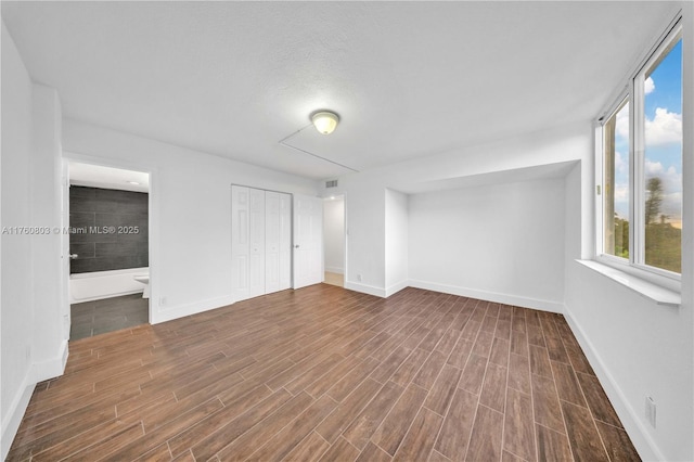 unfurnished bedroom featuring wood finish floors, a closet, baseboards, and ensuite bathroom