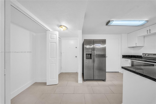 kitchen featuring light tile patterned floors, dark stone counters, white cabinets, appliances with stainless steel finishes, and a textured ceiling