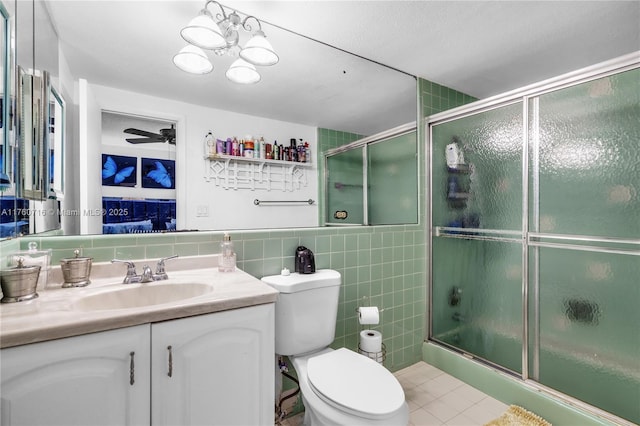 bathroom with toilet, vanity, a shower with shower door, tile patterned floors, and tile walls