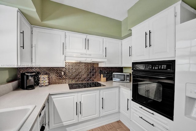 kitchen with under cabinet range hood, backsplash, black appliances, and white cabinets