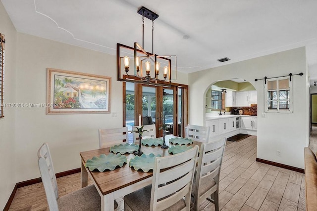 dining room featuring visible vents, a chandelier, a barn door, light wood-style flooring, and arched walkways