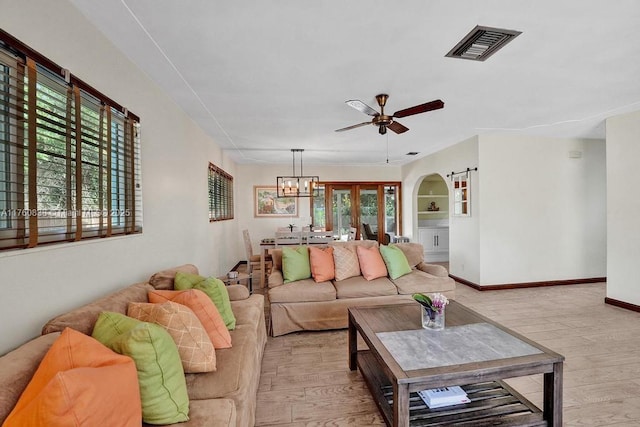 living area with ceiling fan with notable chandelier, visible vents, arched walkways, and light wood finished floors