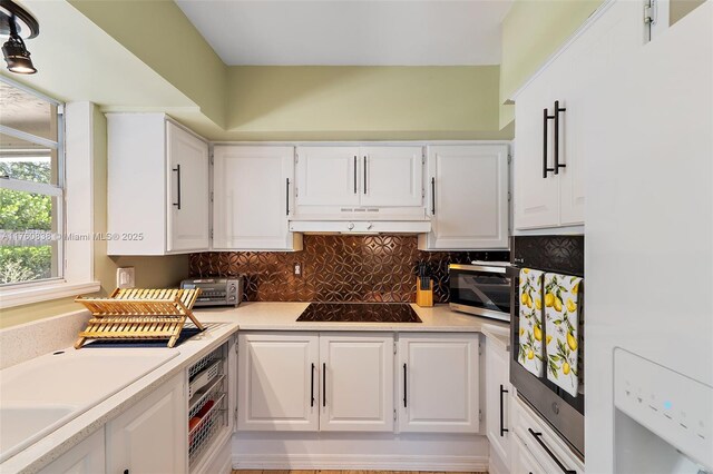 367 W Riverside Dr, Tequesta, FL 33469 - kitchen featuring black electric stovetop, stainless steel microwave, white cabinetry, and under cabinet range hood