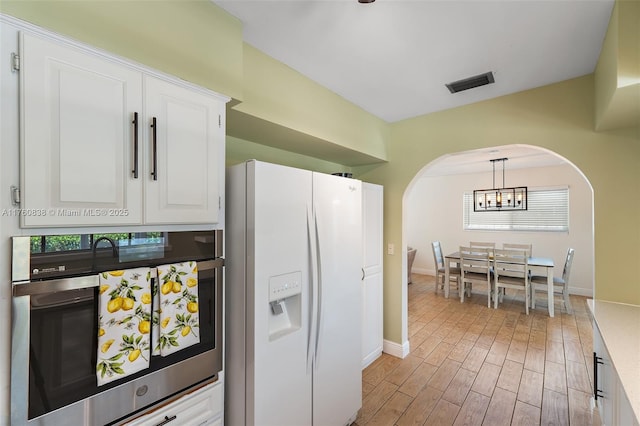 367 W Riverside Dr, Tequesta, FL 33469 - kitchen with white fridge with ice dispenser, arched walkways, a chandelier, white cabinets, and plenty of natural light