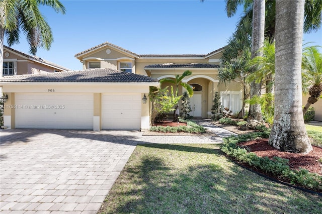 view of front facade featuring a tile roof, a front yard, stucco siding, decorative driveway, and a garage