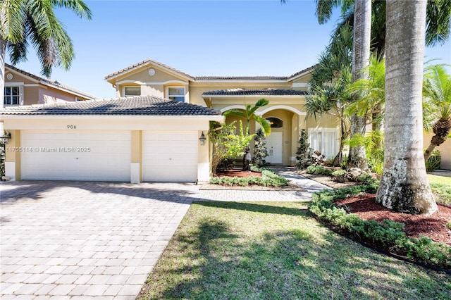 mediterranean / spanish house featuring stucco siding, an attached garage, decorative driveway, and a tiled roof