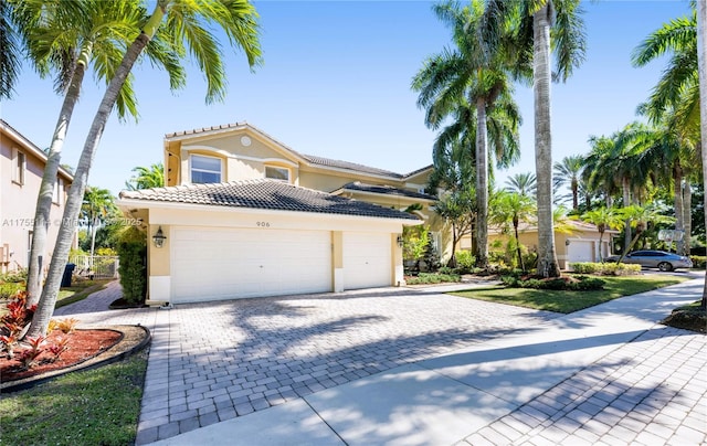 mediterranean / spanish home with a garage, a tile roof, decorative driveway, and stucco siding