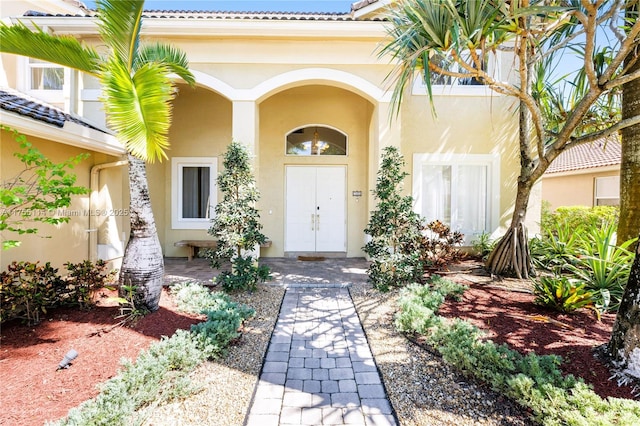 property entrance with stucco siding, a porch, and a tiled roof