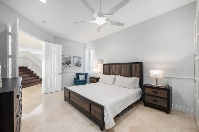 bedroom with a wainscoted wall, marble finish floor, baseboards, and ceiling fan