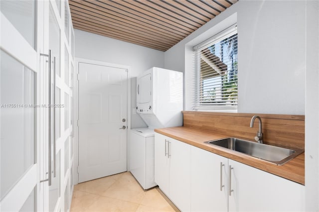 laundry room featuring stacked washer and clothes dryer, light tile patterned floors, cabinet space, and a sink