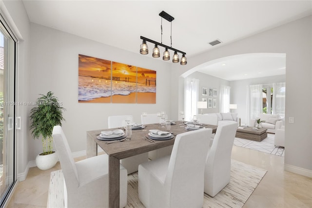 dining room with light tile patterned floors, visible vents, arched walkways, and baseboards