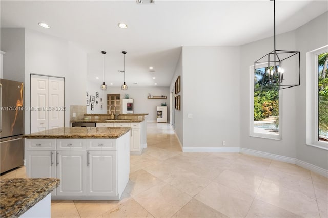 kitchen featuring tasteful backsplash, stone counters, freestanding refrigerator, white cabinetry, and a sink