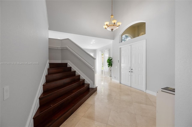 entrance foyer with a towering ceiling, stairway, light tile patterned floors, baseboards, and a chandelier