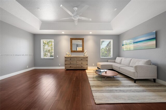 living room with baseboards, a ceiling fan, wood finished floors, and a tray ceiling