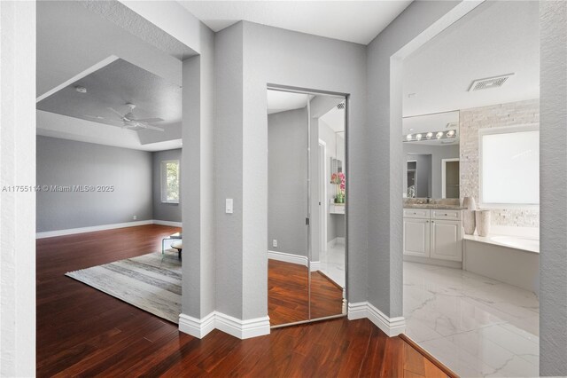 hallway featuring baseboards, wood finished floors, visible vents, and a sink